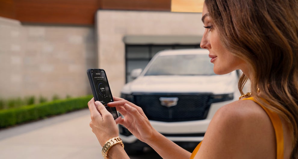 lady checking her mobile with a Cadillac vehicle background | AutoGrupo Cadillac in TOA BAJA PR